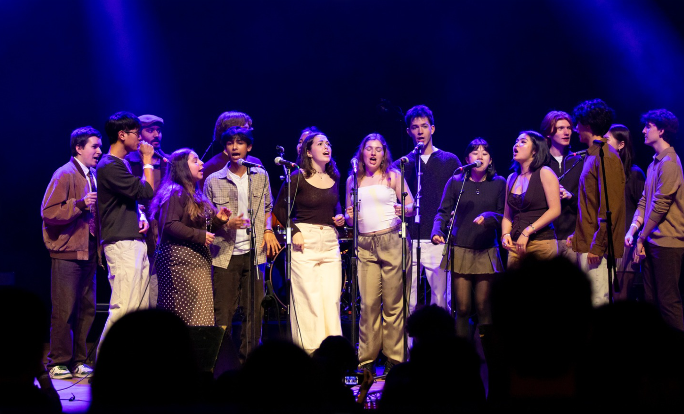 A group of young singers performing on stage with microphones under blue stage lighting.